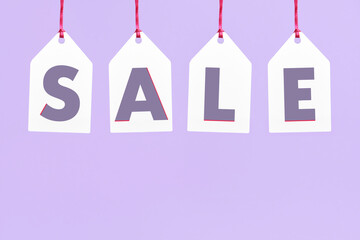 Word Sale written on white paper labels hanging on a pastel lilac background. Simple design with copy space. Concepts: seasonal sales and discounts, black friday advertising campaign.