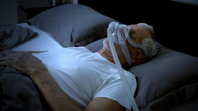 Mature adult sleeping at night while wearing a CPAP mask to treat his Sleep Apnea.