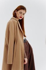 A red-haired lady in a beige coat on a white background. Advertising for brands showrooms catalog of clothing for women