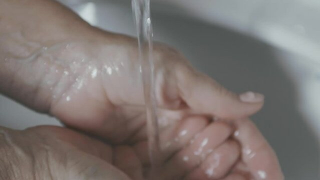 A woman carefully washes her hands under tap water