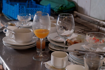 Dirty plates and glasses after a meal in the kitchen in the restaurant. Heap or pile of unclean glass and plates of breakfast or lunch table.