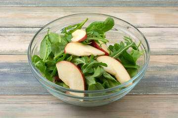 Salad greens and apple slices ingredients in glass bowl as part of meal preparation