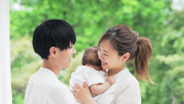 新緑を背景に赤ちゃんを抱っこするカップル　子育てイメージ