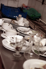 Dirty plates and glasses after a meal in the kitchen in the restaurant. Heap or pile of unclean glass and plates of breakfast or lunch table.