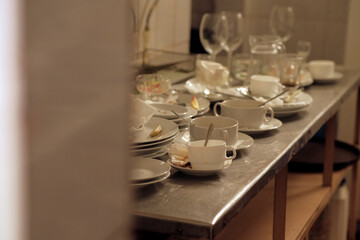 Dirty plates and glasses after a meal in the kitchen in the restaurant. Heap or pile of unclean glass and plates of breakfast or lunch table.