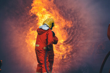 Naklejka premium Firefighter Rescue training in fire fighting extinguisher. Firefighter fighting with flame using fire hose chemical water foam spray engine. Fireman wear hard hat, safety suit uniform for protection
