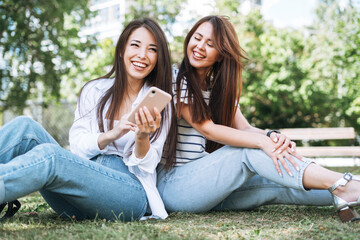 Young asian girls friends using mobile phone having fun in city park