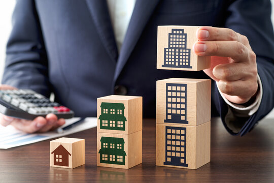 Successful property investment image. Business person calculating rent income and buying property. Stacking wood blocks on table.
