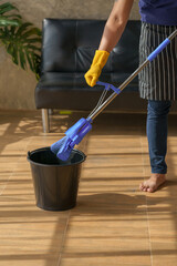 Fototapeta premium Asian young man husband housekeeping using mob cleaning dust on floor at living room.