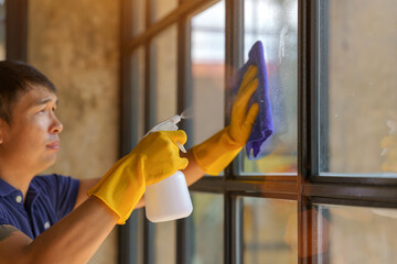 Male professional cleaner in uniform washing window with cotton wiper indoors.