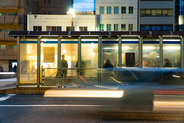 夕暮れの街、路面電車を待つ人々と流れる車