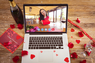 Smiling young biracial woman seen with gift in laptop during video call on valentine day