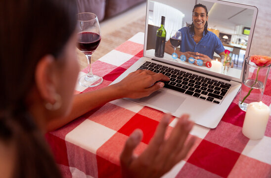 Biracial young couple with red wine dating online through laptop on valentine day