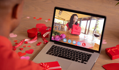 Surprised biracial young woman opening gift during online dating with boyfriend on valentine day - obrazy, fototapety, plakaty