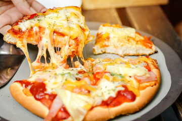 Freshly baked pizza hot from the oven. Slice of hot pizza lunch large cheese topped with tomato sauce and bell pepper vegetables. Italian fast food on a wooden table in side view.