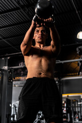 Fototapeta na wymiar Muscular, shirtless Hispanic man lifting a kettlebell as part of his workout at a gym. A Latin man training in the gym. High quality photo