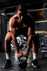 Fototapeta na wymiar Muscular Latin man about to lift a kettlebell. Hispanic man in a dimly lit gym. High quality photo