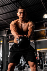 Fototapeta na wymiar Muscular Hispanic man putting in a lot of effort in his training with a kettlebell. A Latin man in a gym working on his arms. High quality photo