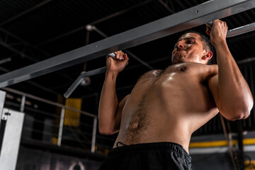 Fototapeta na wymiar Muscular and athletic Latin man working his chest doing pull-ups. A Hispanic man working out his body at the gym. Athletic man doing his training. High quality photo