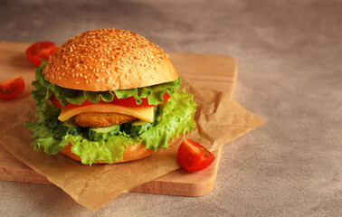 fresh hamburger with cutlet, cucumber, tomato and salad on a wooden board and dark background