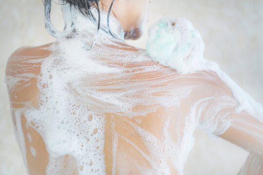 Woman showering. Headshot, Asian woman taking a shower. Cropped image of beautiful naked young woman rubbing body with foam and taking shower in bathroom.

