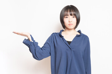 白背景の前で案内のポーズをする若い女性