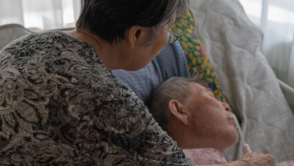 介護用ベッドで眠る高齢者男性に水を飲ませる妻（アップ）