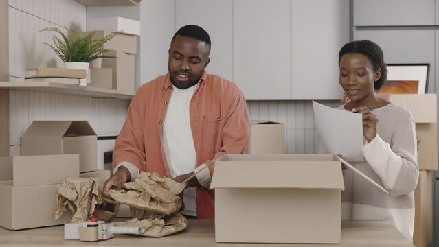 African american couple packing the dishes to the boxes and the woman do the checking list. New home and relocation concept.