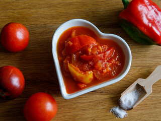 Hungarian delisious homemade lecho with tomato and paprika in sauce in heart shape bowl on wooden background. Vegetarian food close up, top view