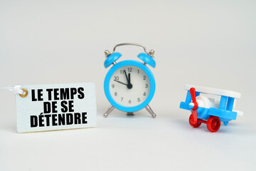 On a white surface there is a toy plane, an alarm clock and a sign with the inscription - time to relax