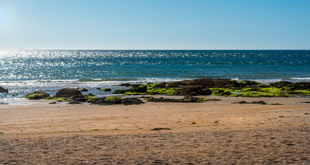 Sunrise view of beach with sand, rocks, sea and clear sky