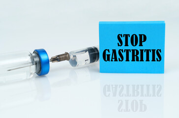 On a white reflective surface there is a syringe with an ampoule and a plate with the inscription - STOP GASTRITIS