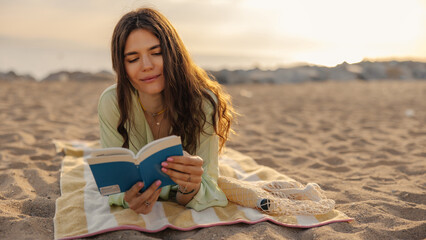 Pretty young attractive woman reading book on the blur background. European brunette lying at beach in morning. Leisure of life concept