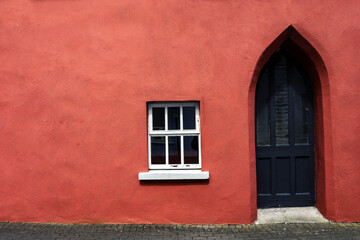 Red color wall and wooden old style black door and white wooden window. Copy space. Exterior of an antique style building. Rich saturated color.