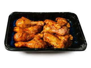Corn fed chicken wings and drumstick in Asian style spicy marinated with herbs in a black plastic tray. Uncooked chicken meat product for barbecue or frying. Isolated on white.