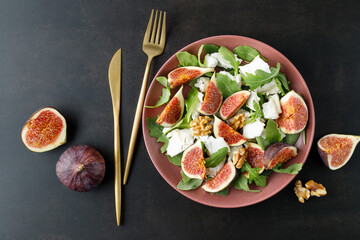 Tasty salad with sliced figs, crushed soft goat cheese, walnut and fresh arugula leaves on red...