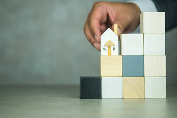 Businessperson hand placing house models on the step of empty wood block. Planning and investment...
