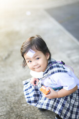 An Asian little girl who wearing a kindergarten uniform and has a wound sewn on her forehead playing alone outside.