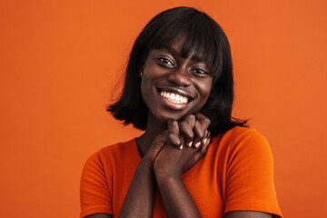 Portrait of cheerful african lady touching chin over orange background