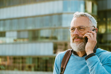 Mature man talking on mobile phone while walking on city street