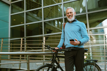 Fototapeta na wymiar Mature man with beard using mobile phone while standing by his bicycle