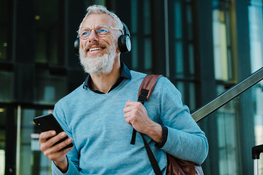 Mature Man Listening Music And Using Mobile Phone By Building At Street