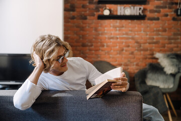 Young handsome relaxed smiling long-haired man in glasses reading book
