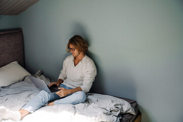 Blonde bristle man working with laptop while sitting on bed at home