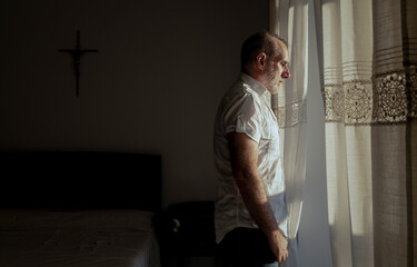 Portrait of adult man standing beside window with sunlight and shadow