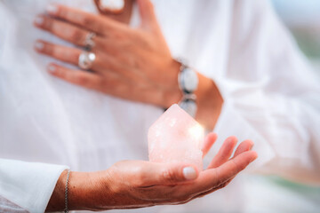 Self-esteem meditation concept. Hand holding a rose quartz crystal, boosting feeling of self-esteem and self-love, improving mood and harmony - obrazy, fototapety, plakaty