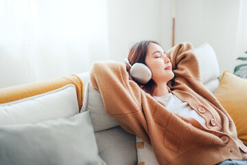 Happy asian woman listening to music from mobile phone while sitting on the the sofa at homes,...