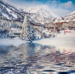 Snowy Valberg village reflected in calm waters of Velbergvika fjord, Lofoten Islands, Norway,...