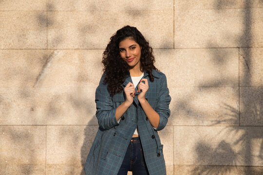 Beautiful young woman with curly brown hair and upturned nose dressed in fashionable clothes poses for photos as a super model on a brown background. Concept of beauty and fashion.