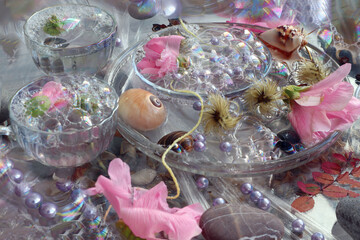  Abstract pastel background: pink mallow flowers, beads, twigs, sea pebbles and a shell in a glass dish among soap bubbles, top view